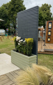 Sage green planter up against a dark grey wooden trellis