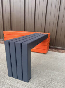 dark grey wooden bench attached to an orange wooden planter