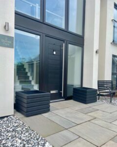 two dark grey square planters outside a glass surrounded front door