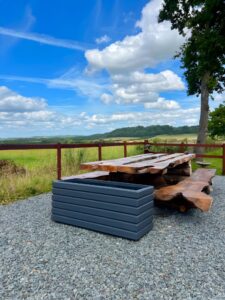 dark grey wooden planter next to a natural wood table outside next to a field