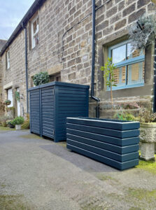 Dark grey planter alongside a double bin store outside a brick wall house